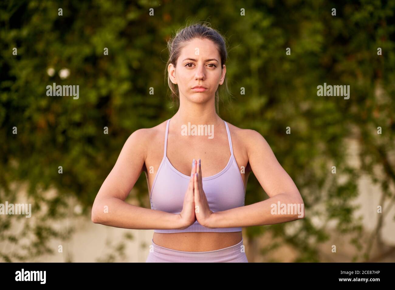 Tranquil female in sports leggings and bra with Namaste hands gesture while doing yoga and looking at camera Stock Photo