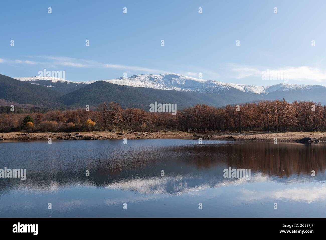 Shore of calm river against snowy autumn mountain ridge and cloudy sky in nature Stock Photo