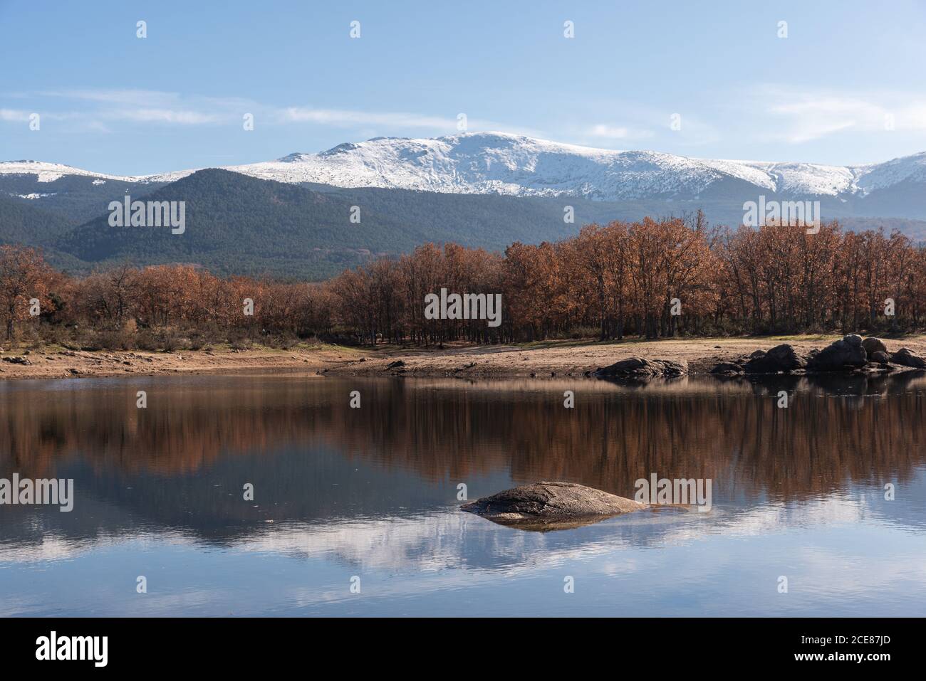 Shore of calm river against snowy autumn mountain ridge and cloudy sky in nature Stock Photo