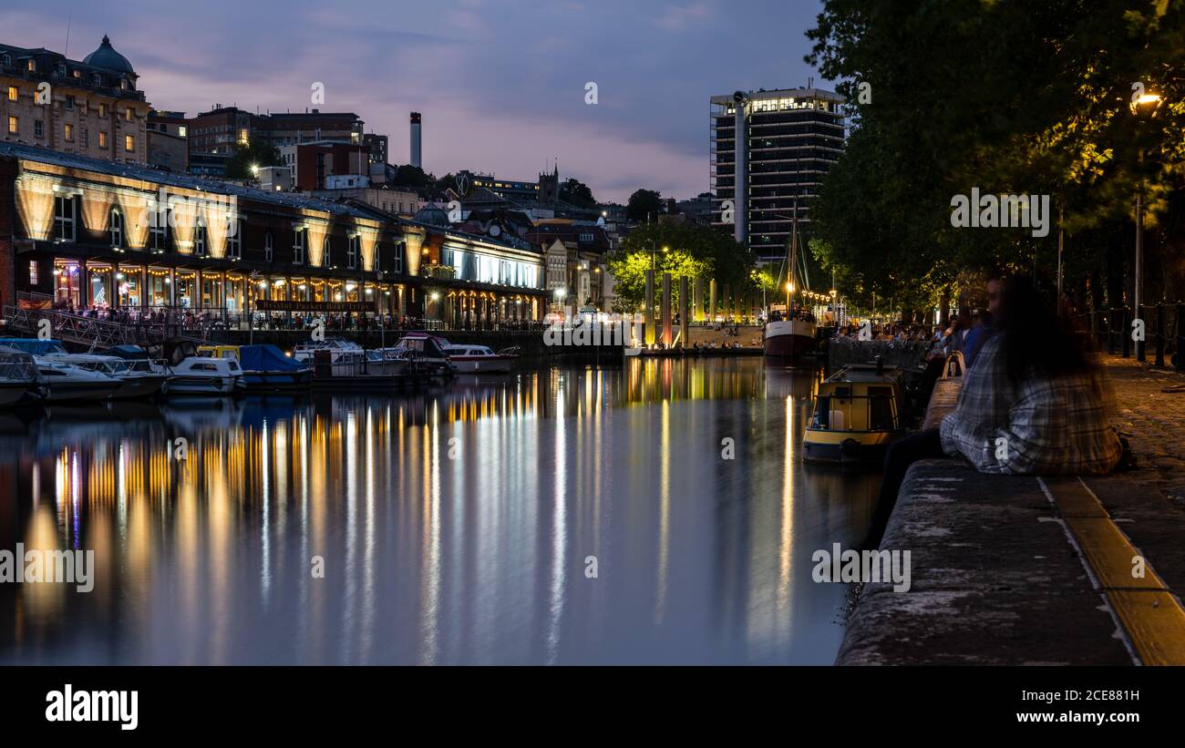 People socialise on the old dock quaysides of Bristol's regenerated post-industrial Harbourside at dusk. Stock Photo