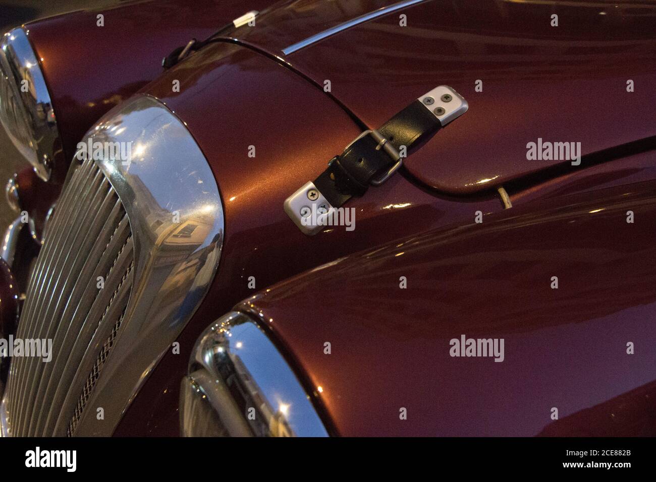 Closeup of a black leather hood strap of a maroon vintage car