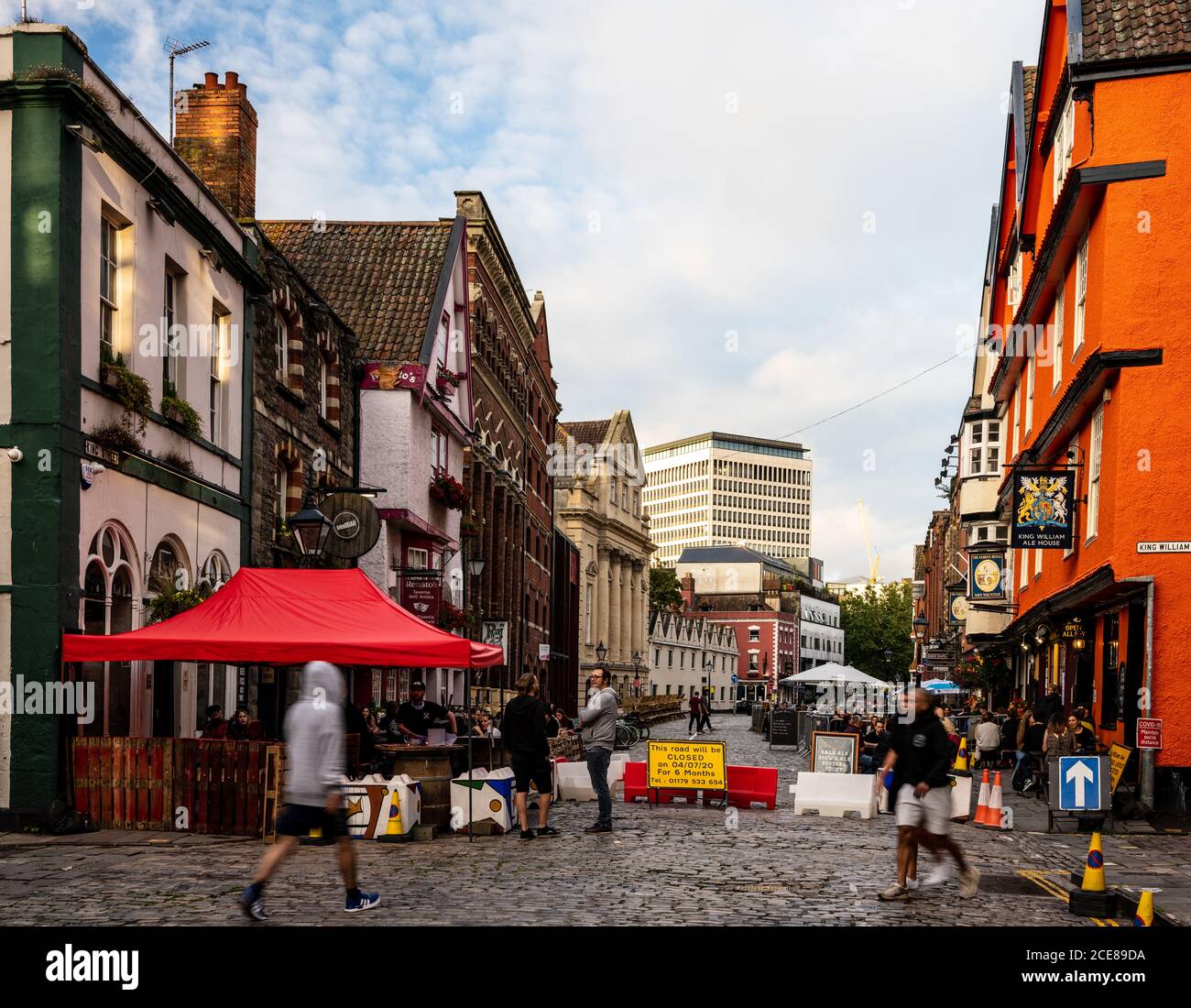 People sit at benches in the street for al fresco dining and drinking outside the bars and restaurants of Bristol's historic King Street during the Cov Stock Photo