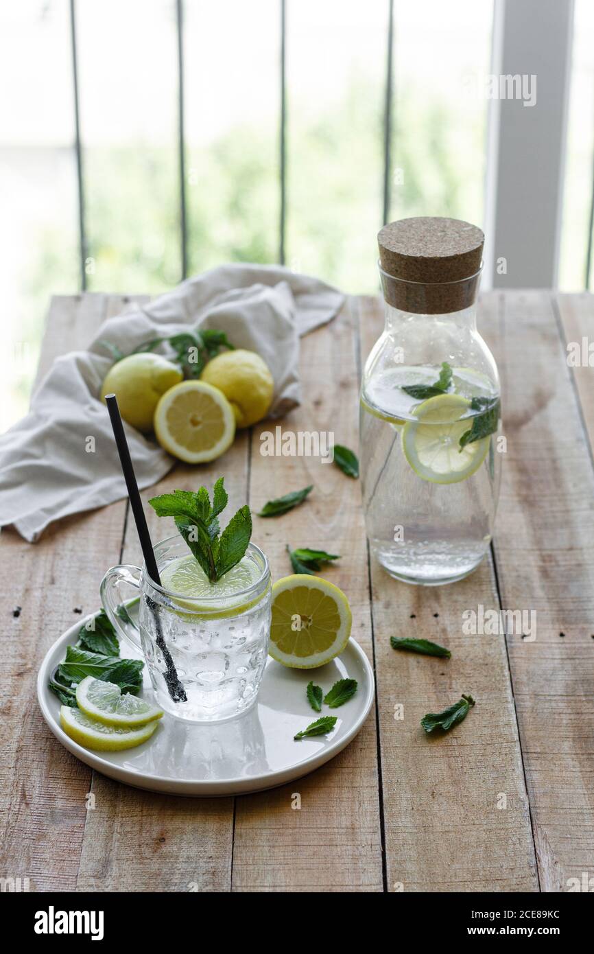 Cold refreshing drink with soda water and lemon garnished with fresh mint leaves served on glass cup with straw on wooden table Stock Photo