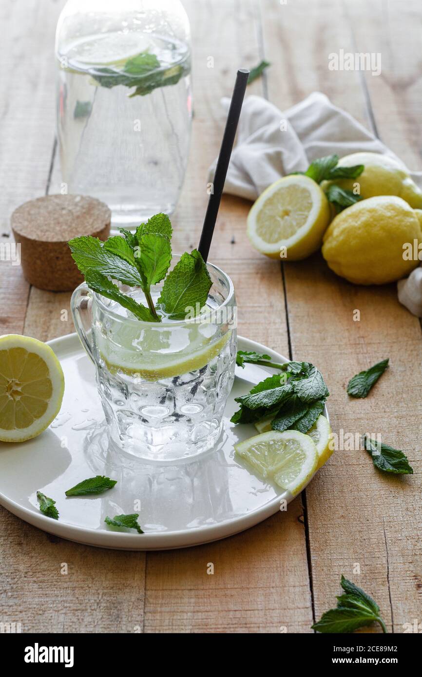 Cold refreshing drink with soda water and lemon garnished with fresh mint leaves served on glass cup with straw on wooden table Stock Photo