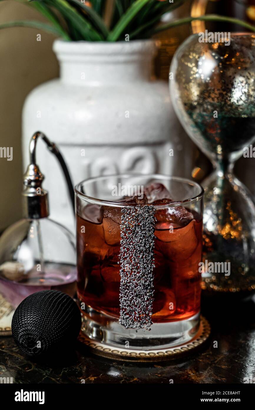 Glass cup of cold alcohol beverage decorated with poppy seeds and placed on table near vintage accessories Stock Photo