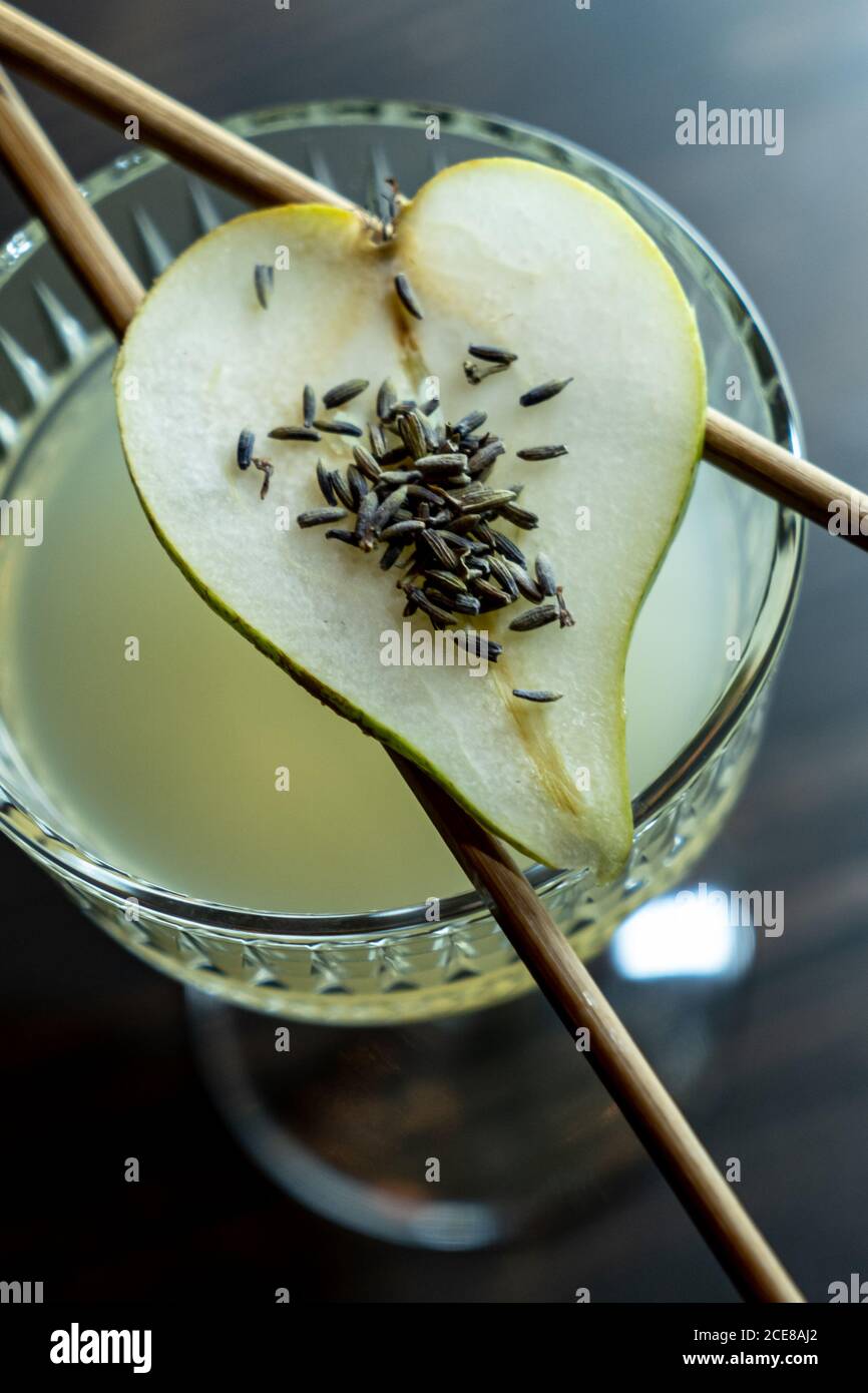 From above half of fresh pear and lavender seeds placed on chopsticks on top of glass with sweet cocktail in bar Stock Photo