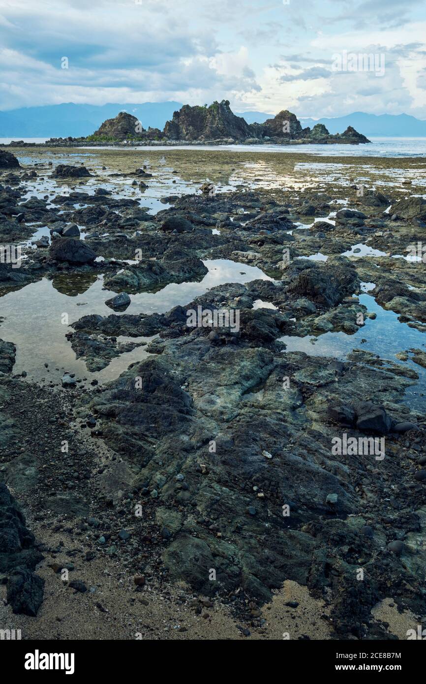 Picturesque scenery of rough stony terrain with sea and high steep rocks under cloudy blue sky Stock Photo