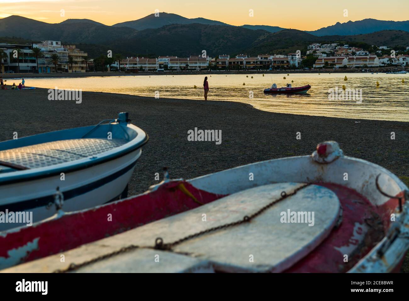 Side view silhouette of anonymous traveler standing on coast with moored fishing boats in calm summer evening in Llanca municipality in Spain Stock Photo