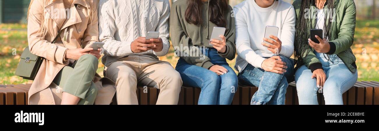 Close up of friends sitting in row and using smartphones Stock Photo