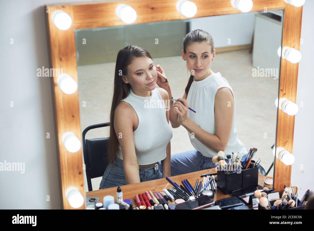 Positive young female makeup artist doing clients face makeup using brush  looking at cozy big mirror with lights in contemporary beauty salon Stock  Photo - Alamy
