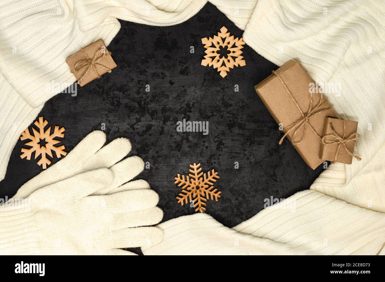 Christmas composition. White scarf, gloves, gift boxes wrapped with kraft paper, wooden snowflakes on black background. Christmas, New Year concept Stock Photo