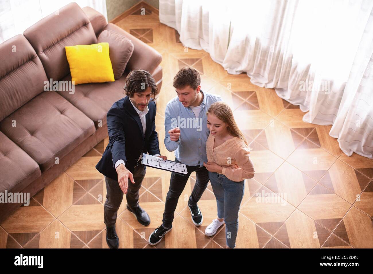 Real estate broker with house plan showing young married couple around