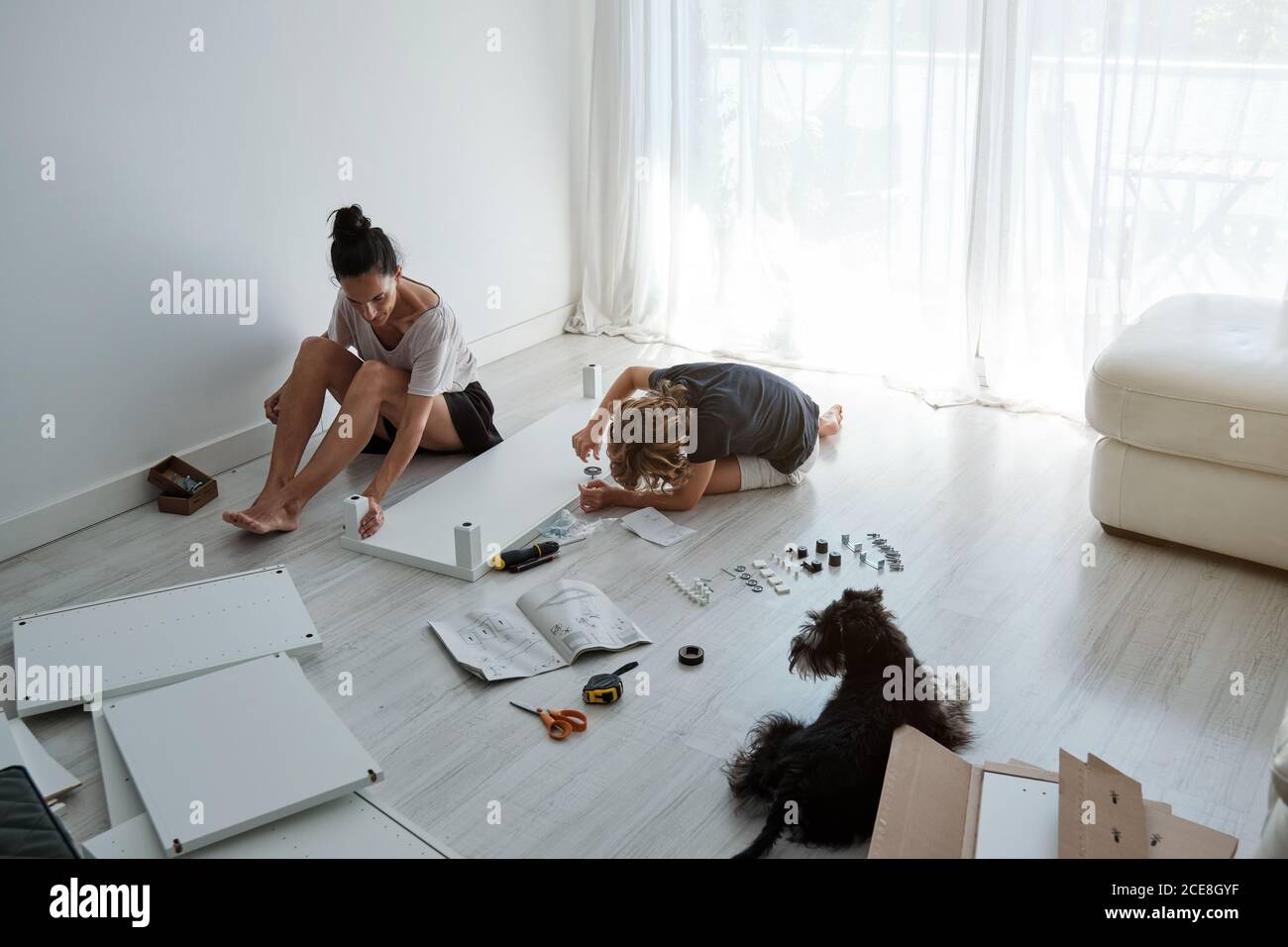 Preteen boy helping mother with fixing new wardrobe in light room with dog Stock Photo