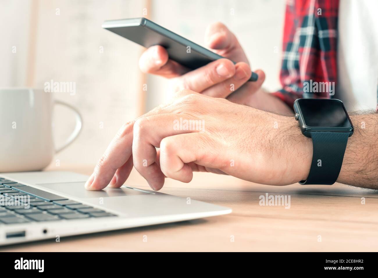 Freelancer using smartphone and laptop computer in home office while telecommuting, selective focus Stock Photo