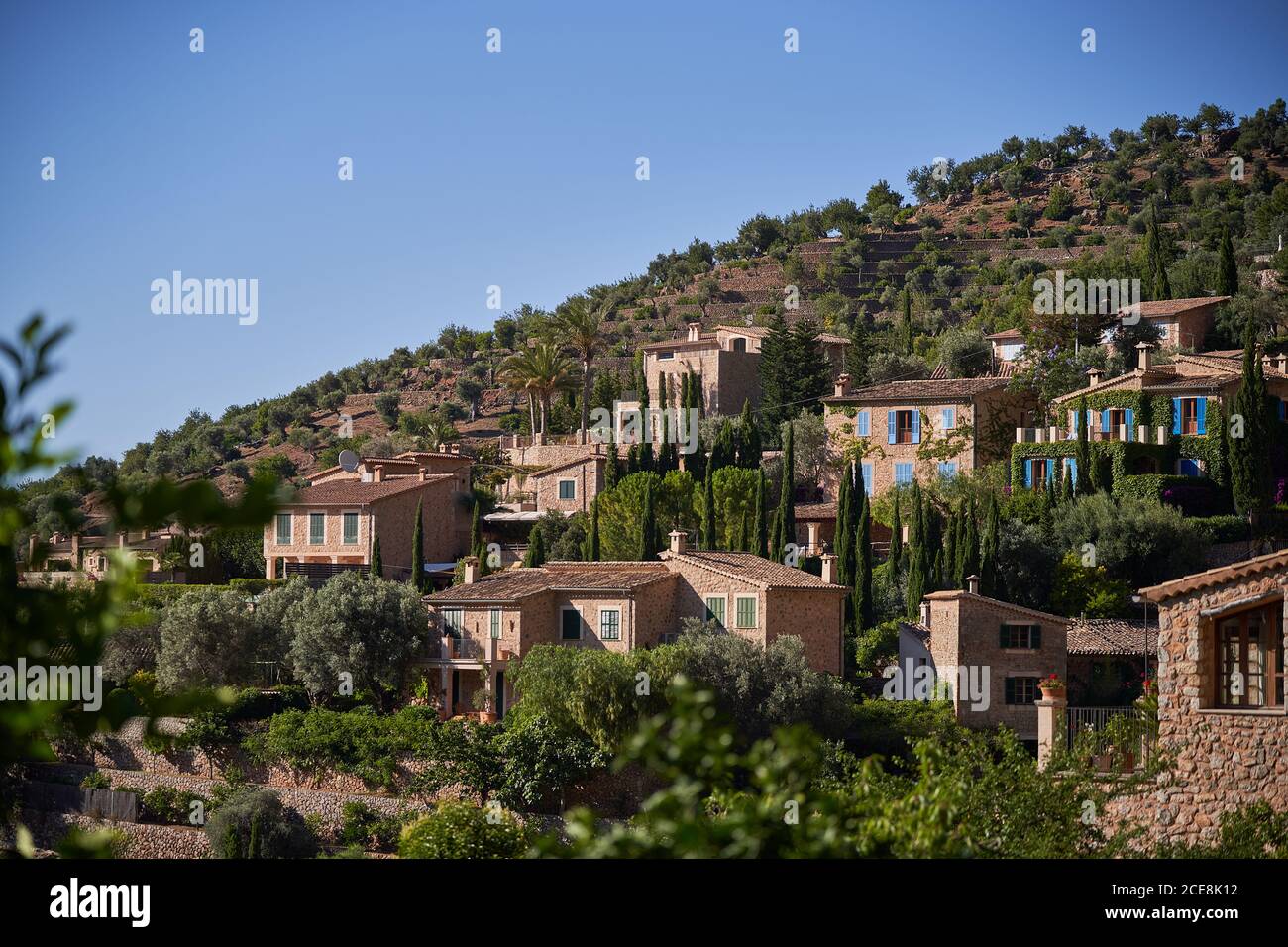 Picturesque view of ancient settlement with small stone houses located on green hill against cloudless blue sky in sunny summer day Stock Photo