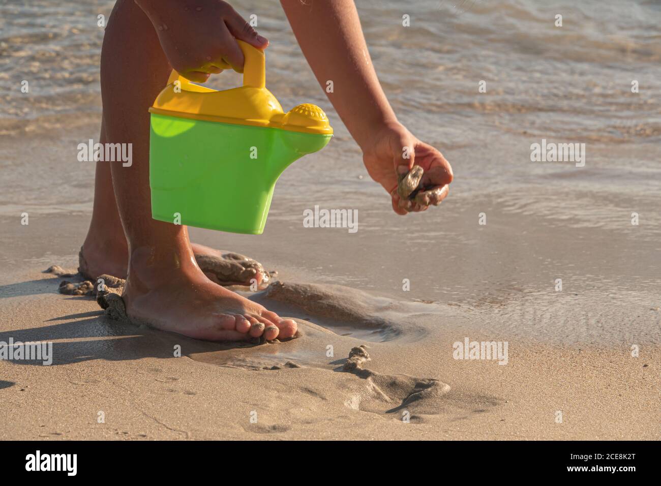Little kid playing with bucket toys and walking on the beach at sunset