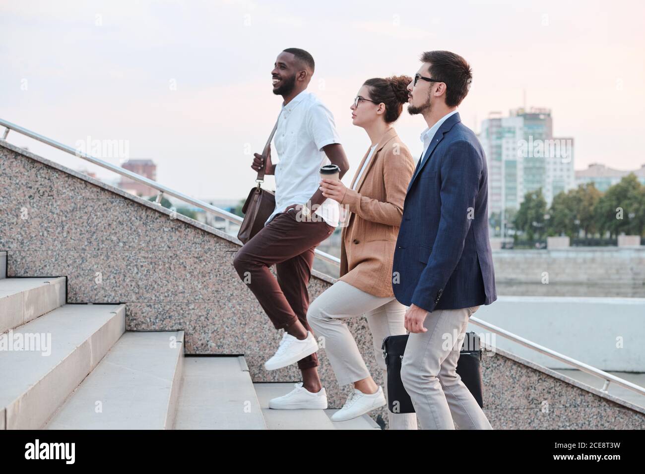 Side view of confident multi-ethnic students chatting and moving up stairs while walking into university Stock Photo