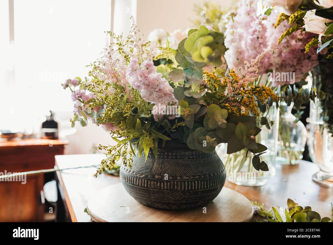 Beautiful bouquet with various flowers including craspedia flowers with green eucalyptus branches arranged in ornamental ceramic pot placed on table in creative floristry studio Stock Photo