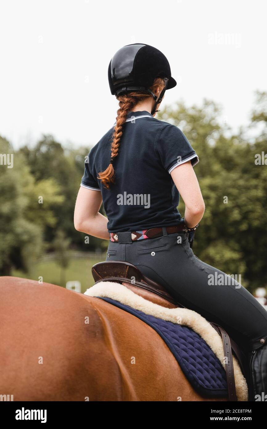 Back view of unrecognizable female equestrian riding chestnut horse during dressage in park Stock Photo