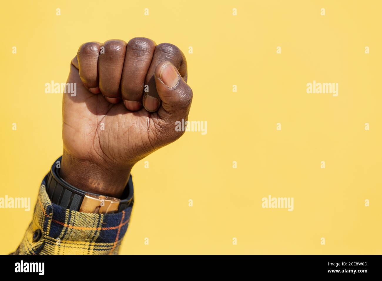 raised fist of a black man on an intense yellow background, concept of human rights struggle and lifestyle, copy space for text Stock Photo