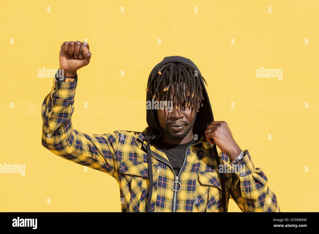 attractive young black man with raised fist and hood on an intense yellow background, concept of human rights struggle and lifestyle, copy space for text Stock Photo