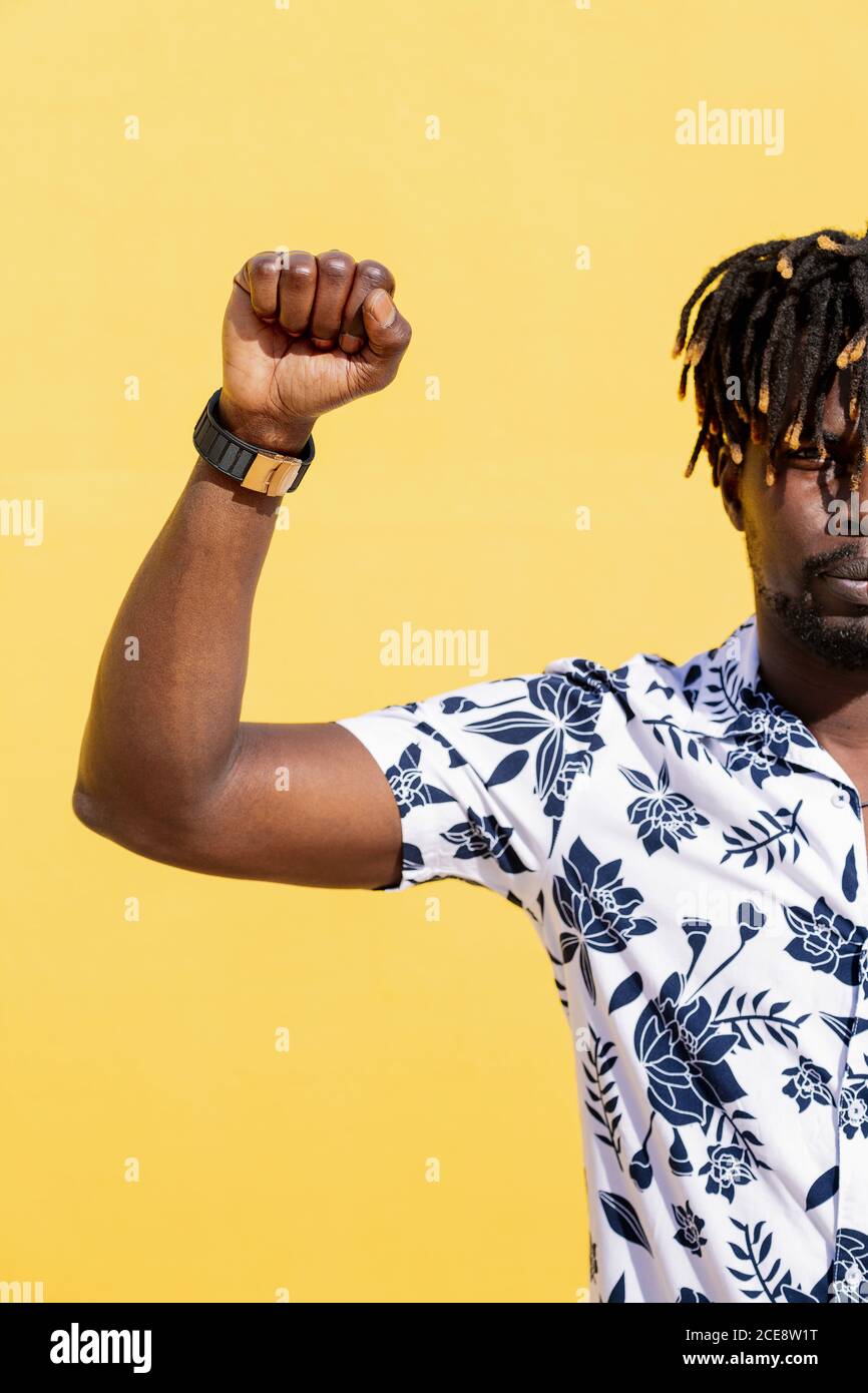 vertical photo of an attractive young black man with raised fist on an intense yellow background, concept of human rights struggle and lifestyle, copy space for text Stock Photo