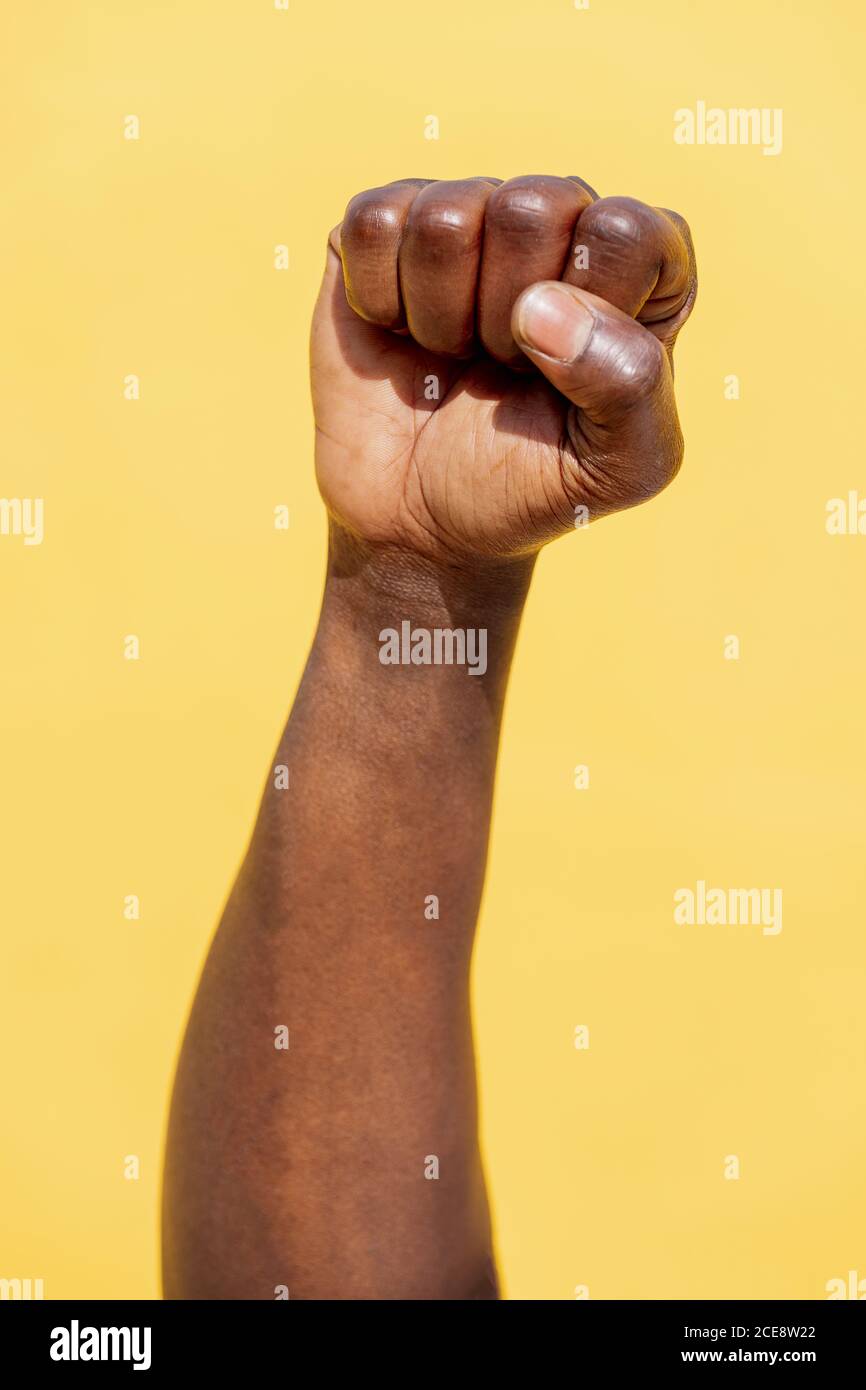 vertical photo of a raised fist of a black man on an intense yellow background, concept of human rights struggle and lifestyle Stock Photo