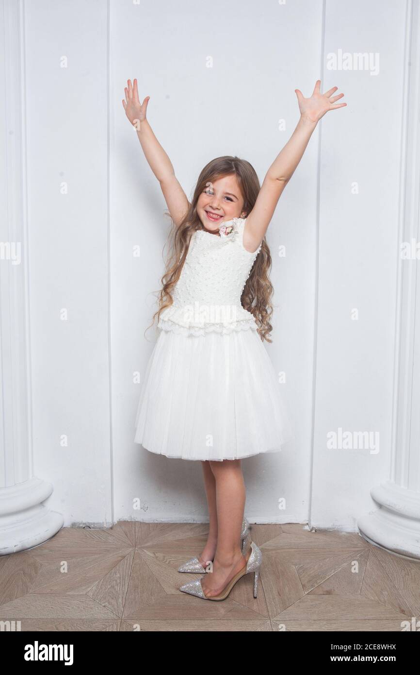 Little princess - excited emotional cute girl in fashion white dress having  fun and wearing big mothers sparkle high heels shoes on white background  Stock Photo - Alamy