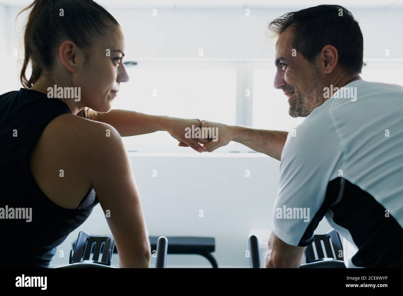 Side view of content female athlete giving fist bump to personal male instructor in modern fitness club Stock Photo