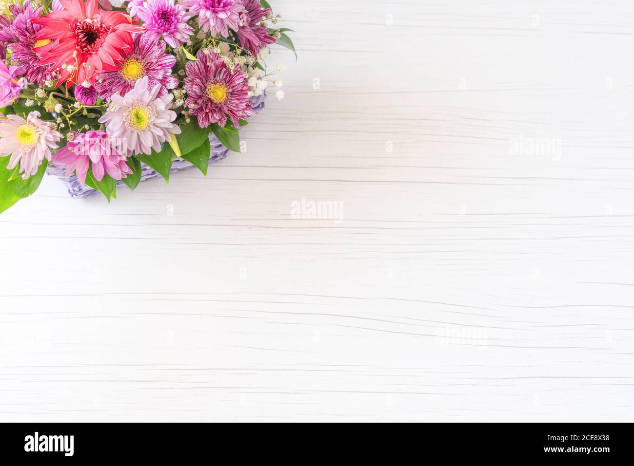 Beautiful bouquet of bright flowers in basket on white wooden background. Stock Photo