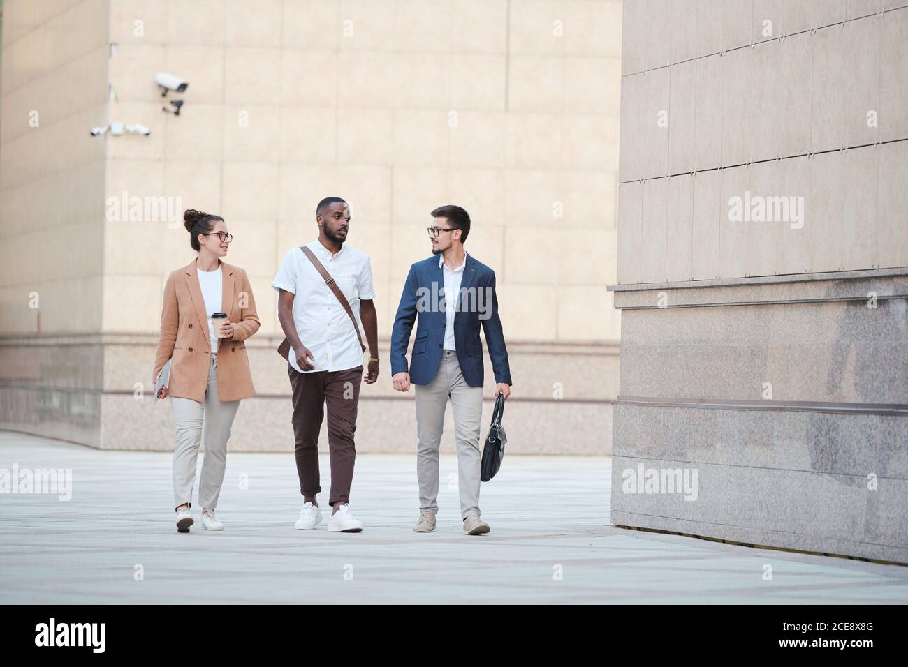 Confident young business specialists walking over business district and talking about project promotion on move Stock Photo