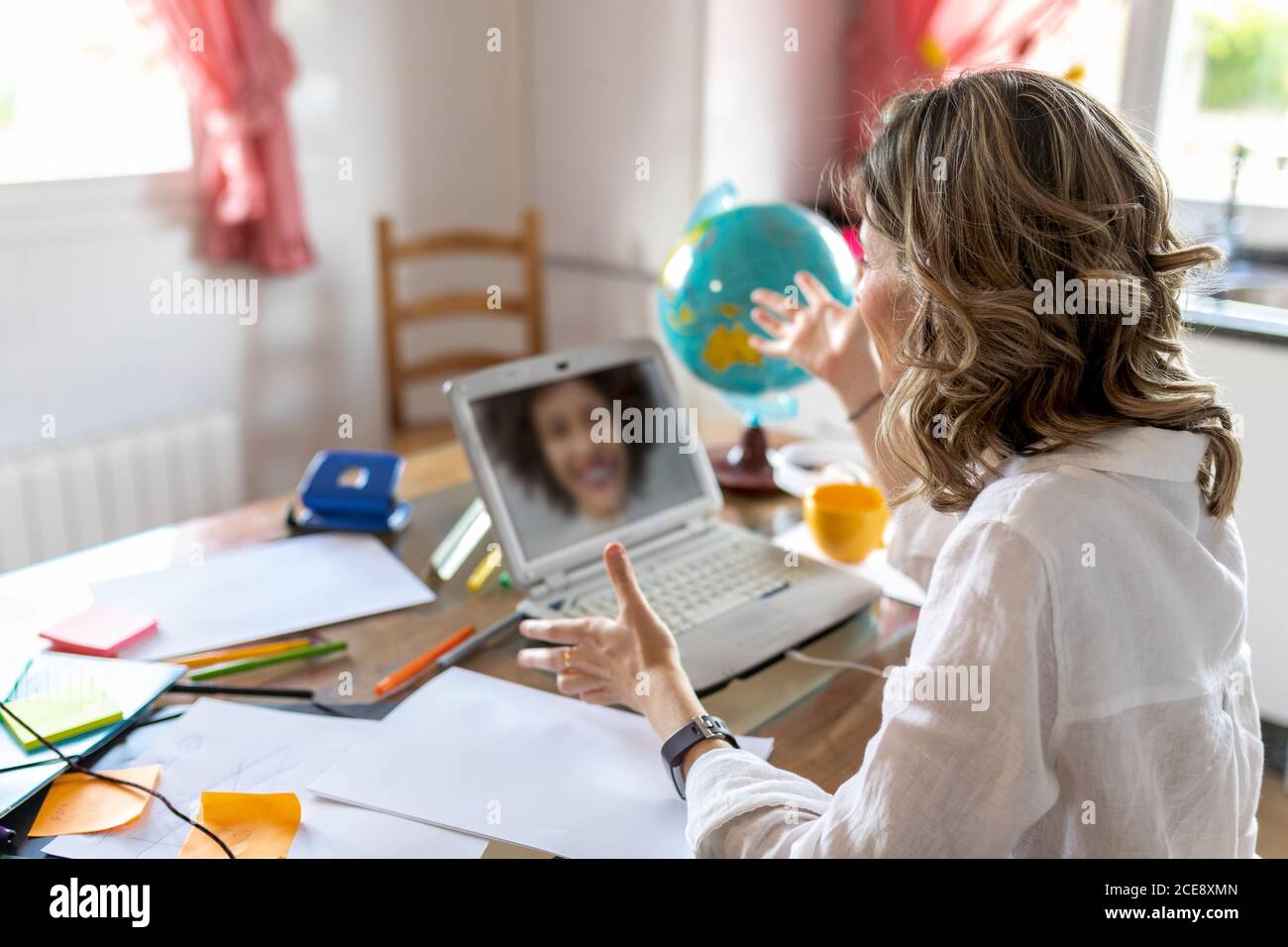 From above side view of anonymous female speaking with friend while having video chat on netbook and sitting with hands apart at table with stickers and colorful stationery in flat Stock Photo