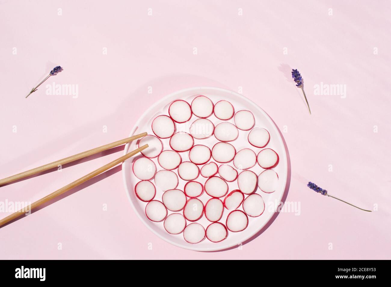 Top view of circles of fresh radish placed on plate with wooden chopsticks and lavender flowers Stock Photo