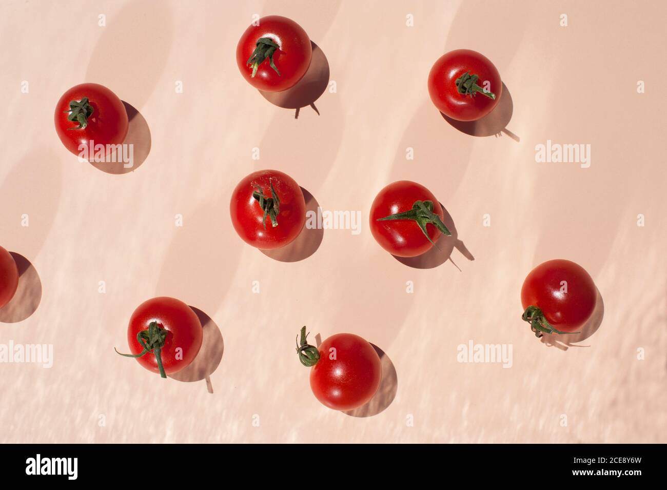 Top view of bunch of ripe red cherry tomatoes with green stems placed on beige background Stock Photo