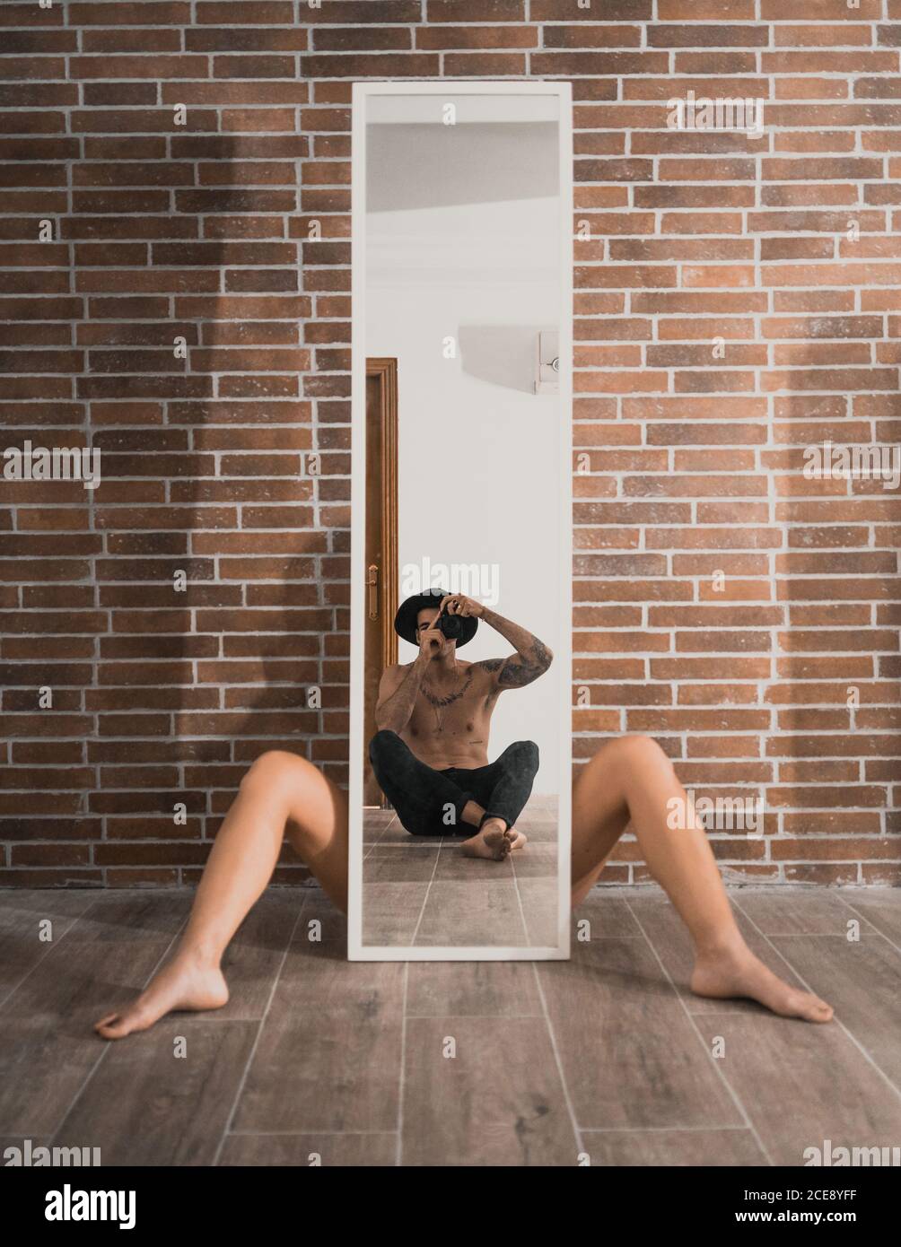 Stylish boyfriend taking provocative photo of girl sitting with legs apart on floor behind