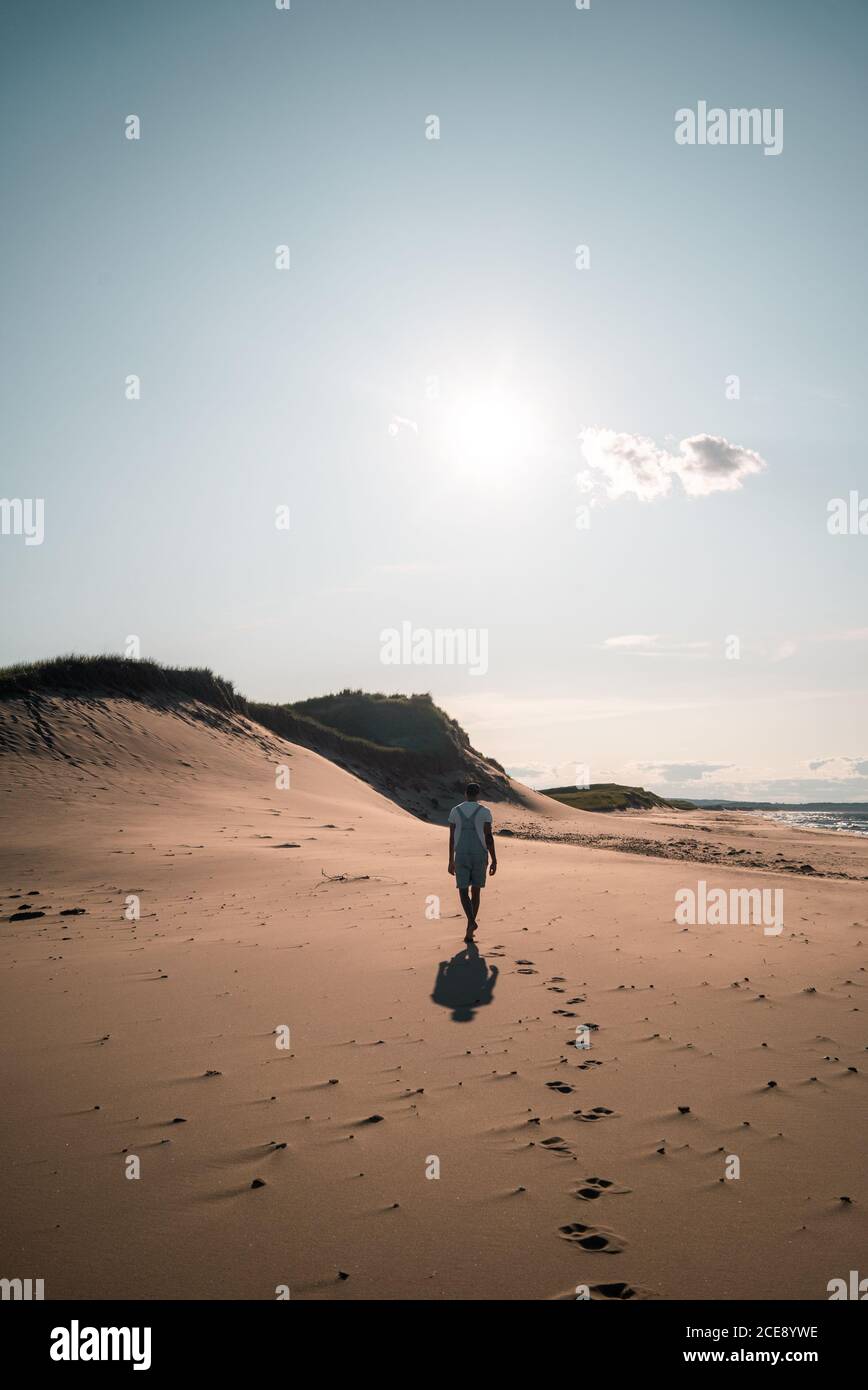 Back view of anonymous male tourist in summer clothes walking barefoot along sea during vacation Stock Photo