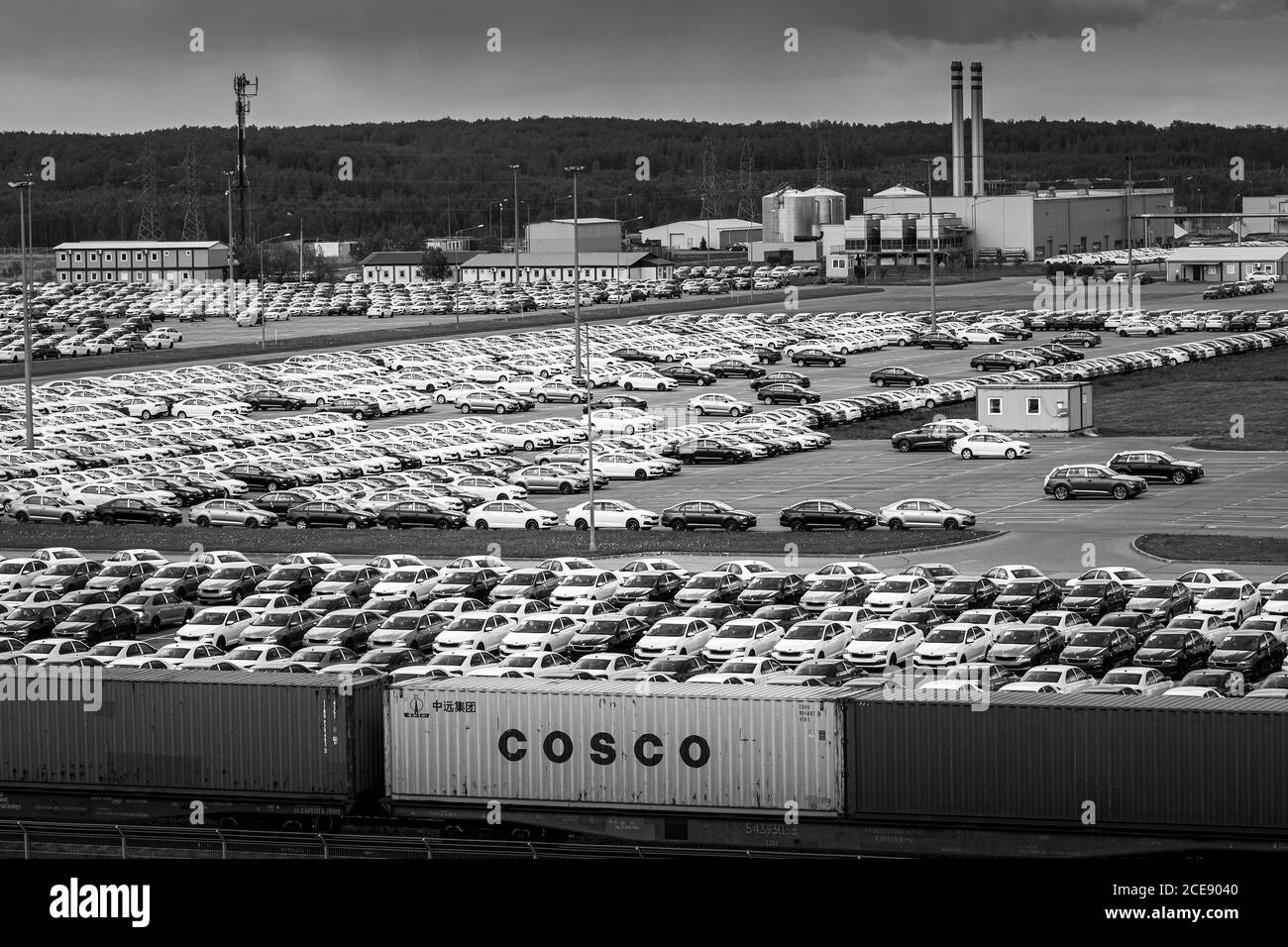 Volkswagen Group Rus, Russia, Kaluga - MAY 24, 2020: Rows of a new cars parked in a distribution center with train on a foreground and car factory on Stock Photo