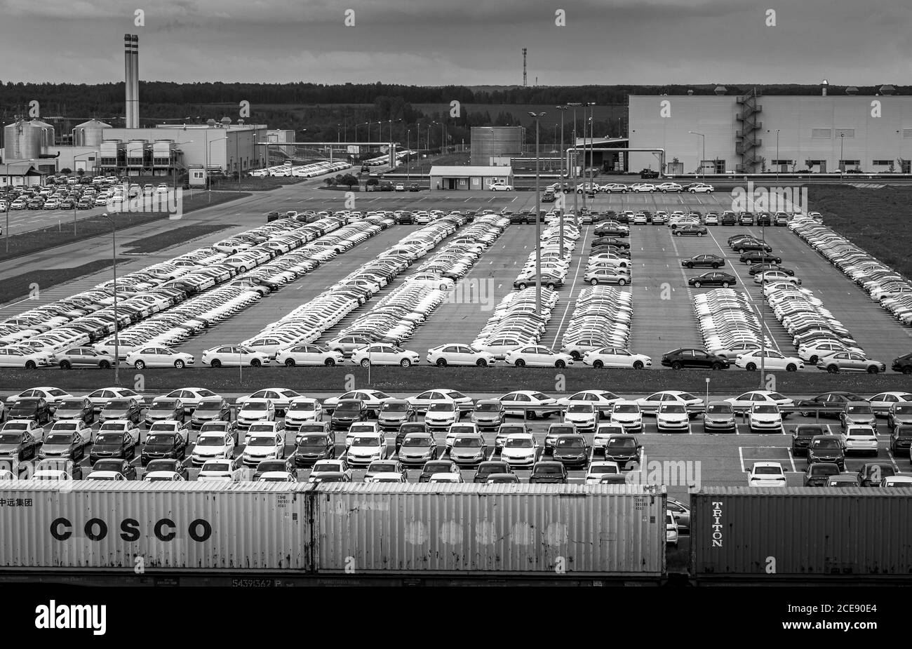 Volkswagen Group Rus, Russia, Kaluga - MAY 24, 2020: Rows of a new cars parked in a distribution center with train on a foreground and car factory on Stock Photo