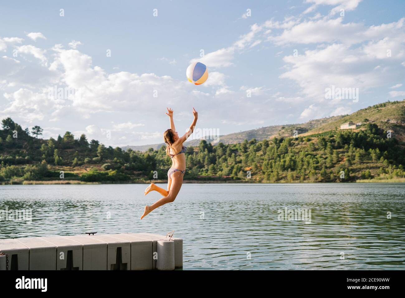 Side view of girl in bikini playing with beach ball and jumping in water of  pond during summer holiday Stock Photo - Alamy