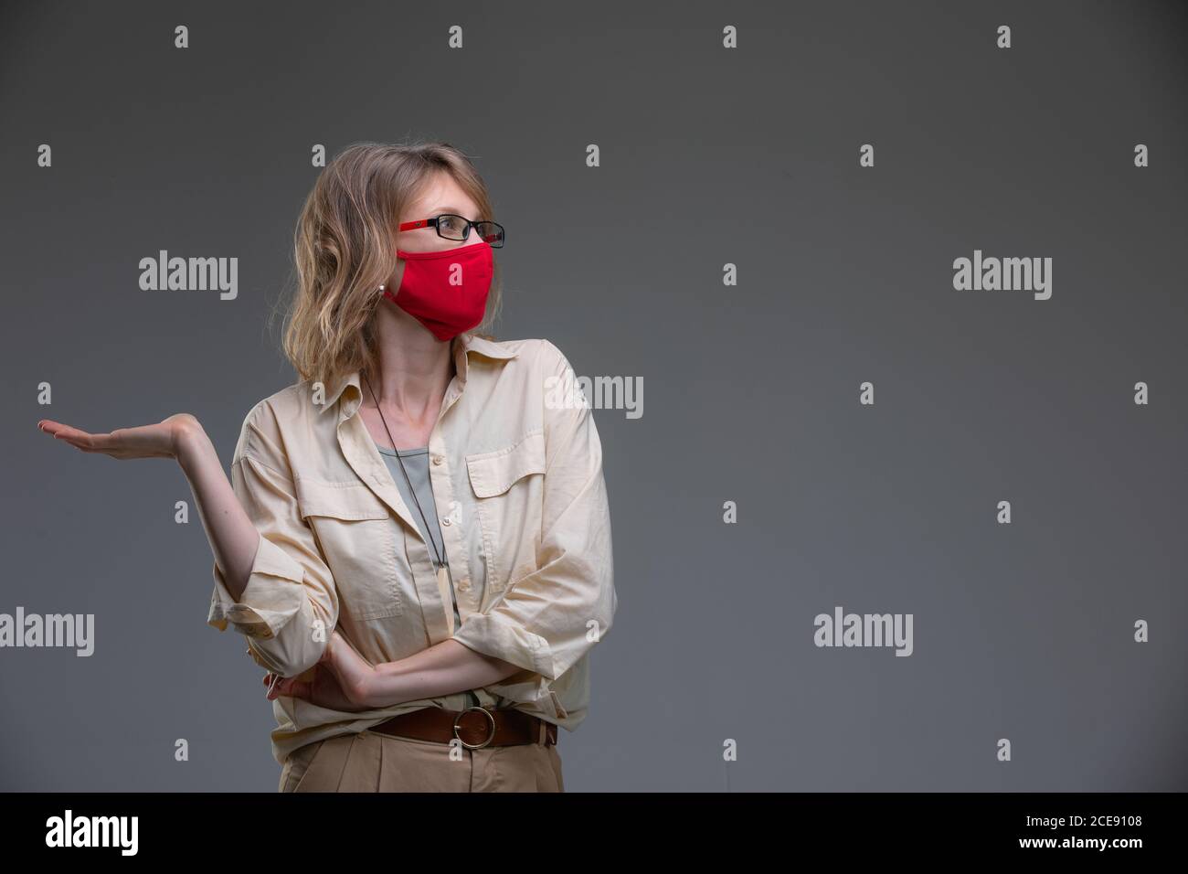 Blond young female in red protective mask against viruses, holds her head. Stock Photo