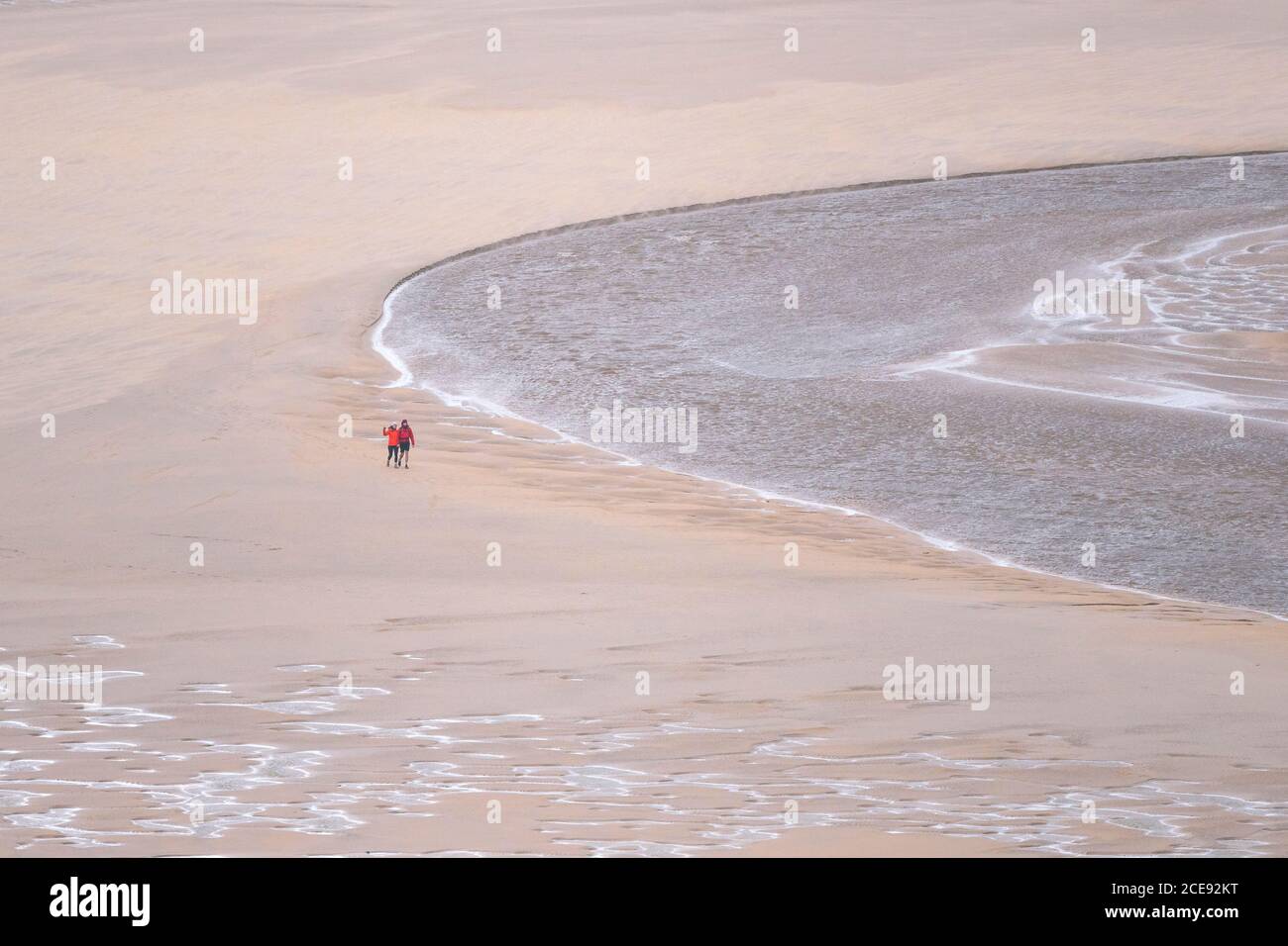 Walkers seen from a distance walking at low tide across Crantock Beach as the River Gannel flows to the sea in Newquay in Cornwall. Stock Photo