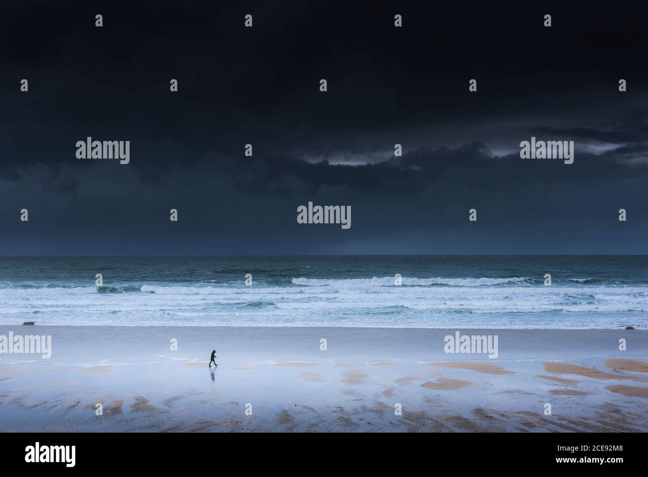Dark storm clouds approaching the coast as a small figure walks along the shoreline of Fistral Beach in Newquay in Cornwall. Stock Photo