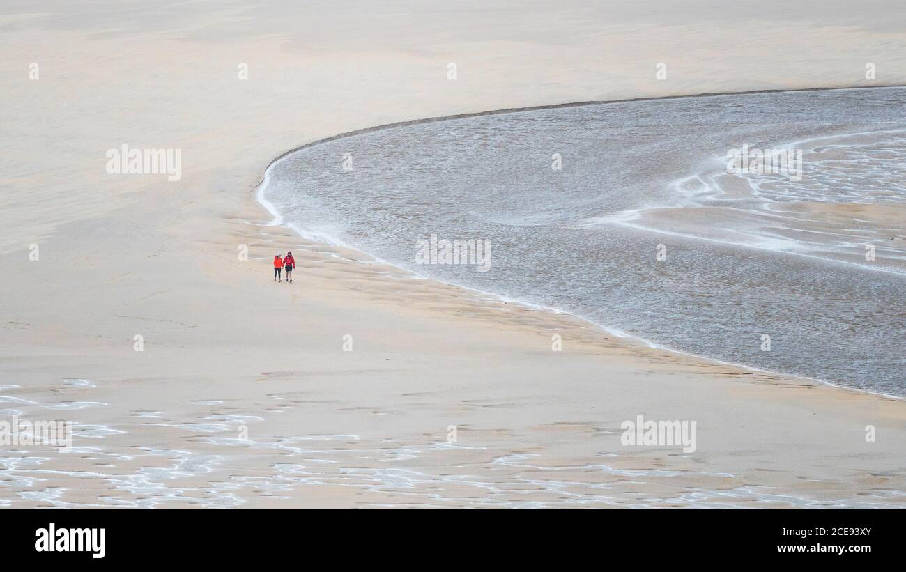 A panoramic image of walkers seen from a distance walking at low tide across Crantock Beach in Newquay in Cornwall. Stock Photo
