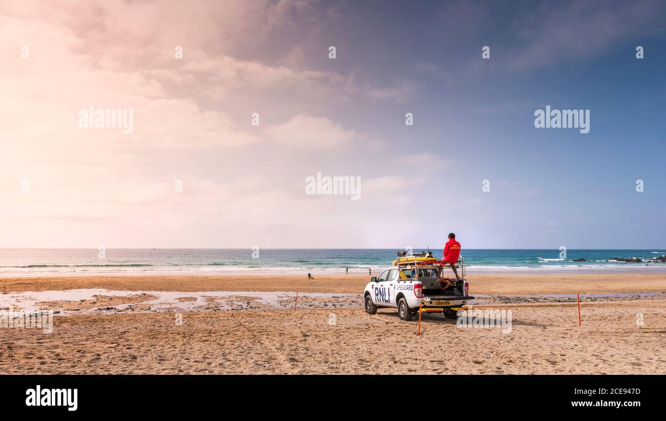 A panoramic view of a RNLI Lifeguard on duty standing on the back of an emergency response vehicle on Fistral Beach in Newquay in Cornwall Stock Photo