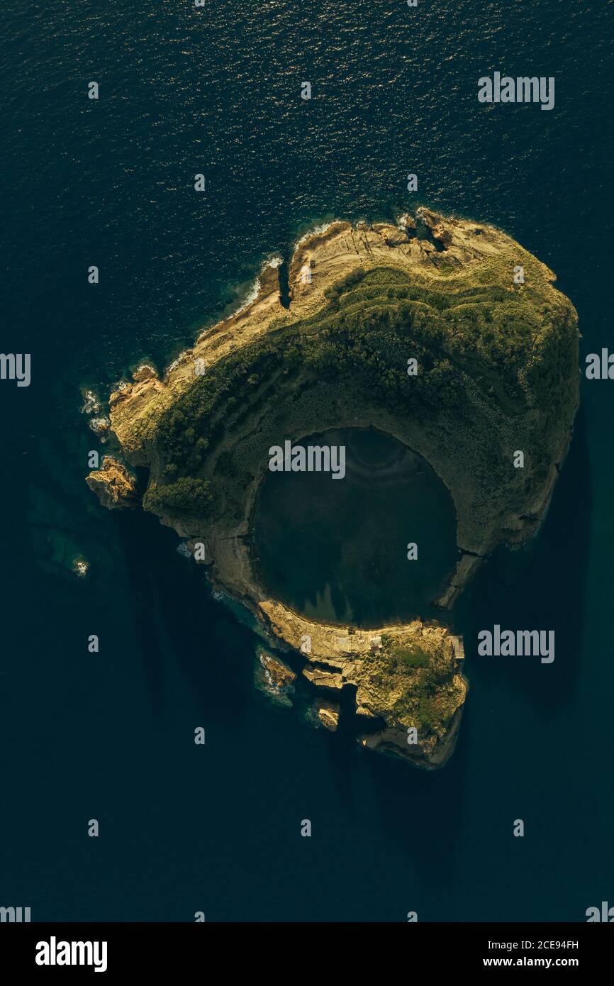 Aerial view of little rocky island washed by calm blue sea at daylight