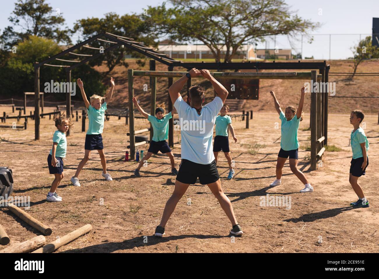 Male fitness coach and kids performing jumping jacks at a bootcamp Stock Photo