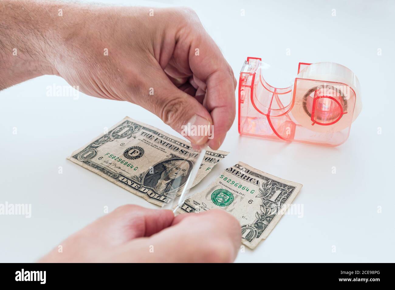 close-up of hands of man fixing old torn dollar bill with sticky tape on white desk Stock Photo