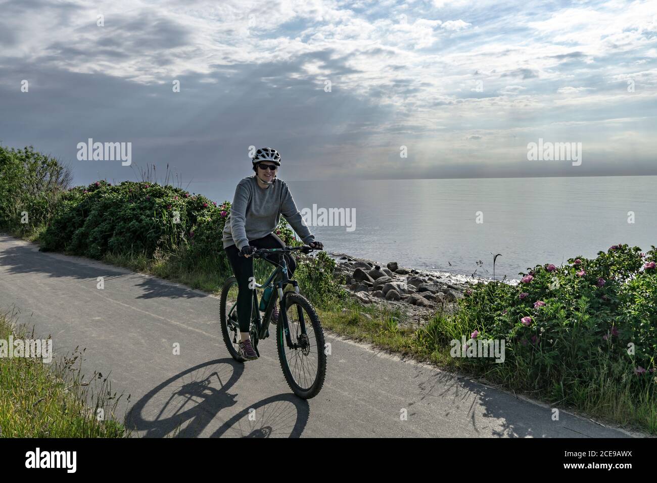 Young woman cyclist riding bicycle along the coastm, Baltic Sea Stock Photo