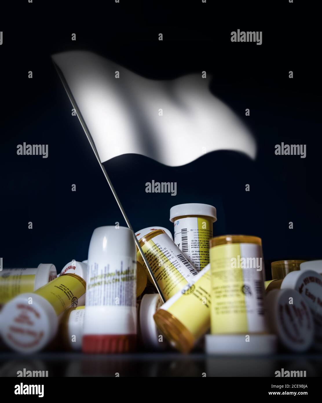 In the center of a pile of pills containers and other drugs, a white flag rises. Stock Photo
