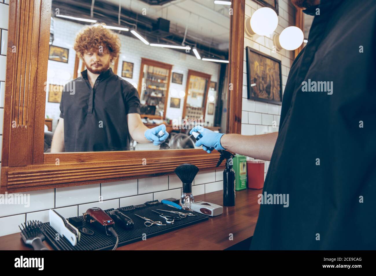 Male caucasian barber at the barbershop wearing gloves preparing working place for client. Professional barber wearing gloves. Covid-19, beauty, selfcare, style, healthcare and medicine concept. Stock Photo